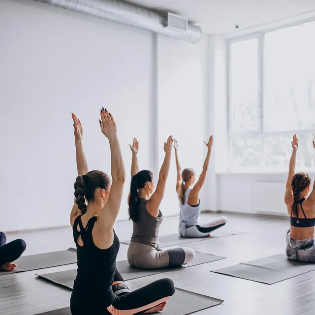 Yogaklasse med armer hevet i synkron øvelse, i lys studio.