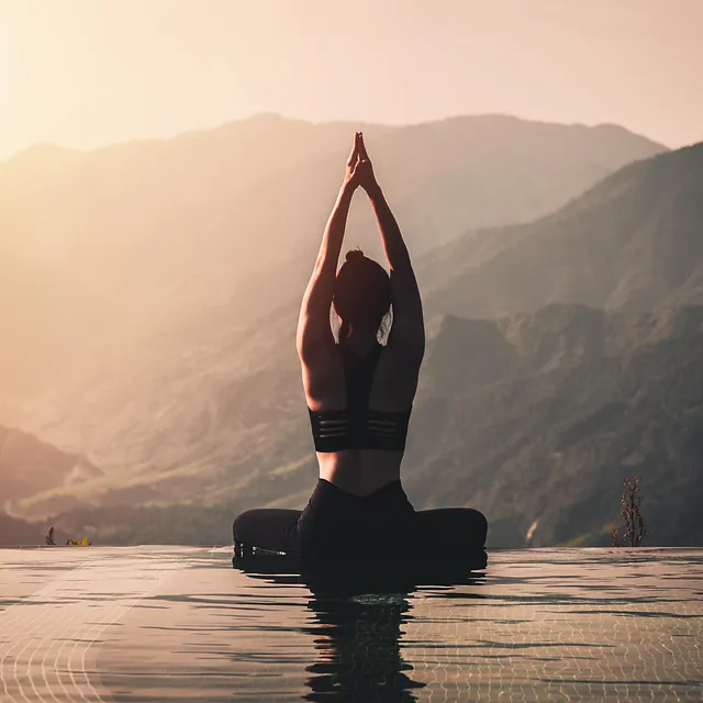 Kvinne i yoga stilling ved bassengkant, fjell i solnedgang bak.